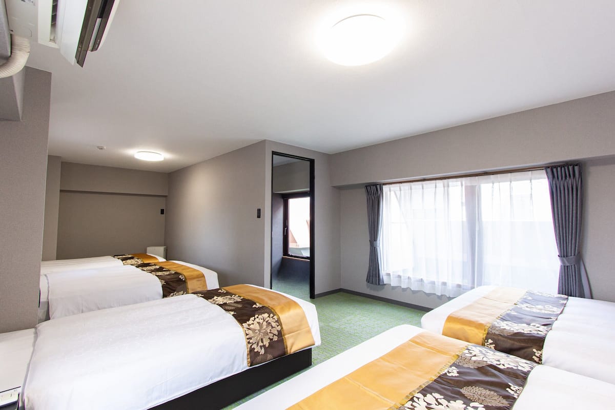 A hotel room with two beds, a large window with curtains, a door leading to a balcony, and a ceiling light.