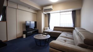 A modern hotel room with a large sofa, a flat-screen TV, a coffee table, and a large window with curtains. - THE LANG HOTEL (Fukuoka)