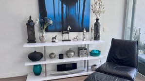 A modern living room with a large flat-screen TV mounted on a white wall, a black leather chair, and a wooden floor.