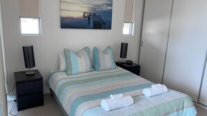 A neatly arranged bedroom with a bed, two bedside tables, a wall-mounted lamp, and a painting above the bed.