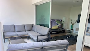 A modern living room with a grey sectional sofa, a glass coffee table, and a TV displaying a racing game.