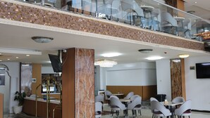 A modern hotel lobby with a glass balustrade, marble columns, and a mezzanine level with seating.
