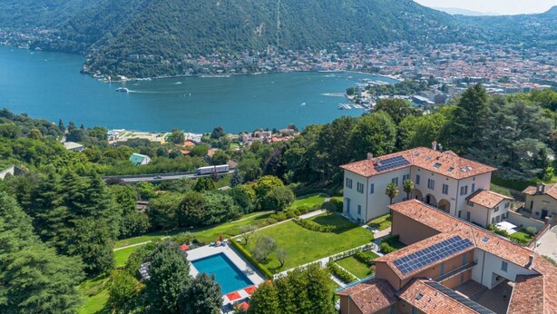 Una località costiera con una vasta distesa d'acqua, una collina con edifici e una villa dotata di pannelli solari.
