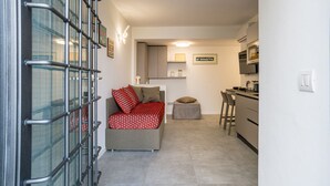 Un ambiente compatto con angolo cottura, un divano con cuscini decorati e un piccolo sgabello.