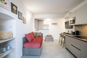A compact living space with a kitchenette, a sofa, a small table, and a chair.