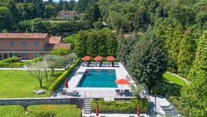 Una piscina con ombrelloni rossi, circondata dal verde e da un muro in pietra.