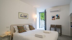 Una camera d'albergo con un letto, un comodino, una lampada da lettura, una finestra vista e un condizionatore d'aria.