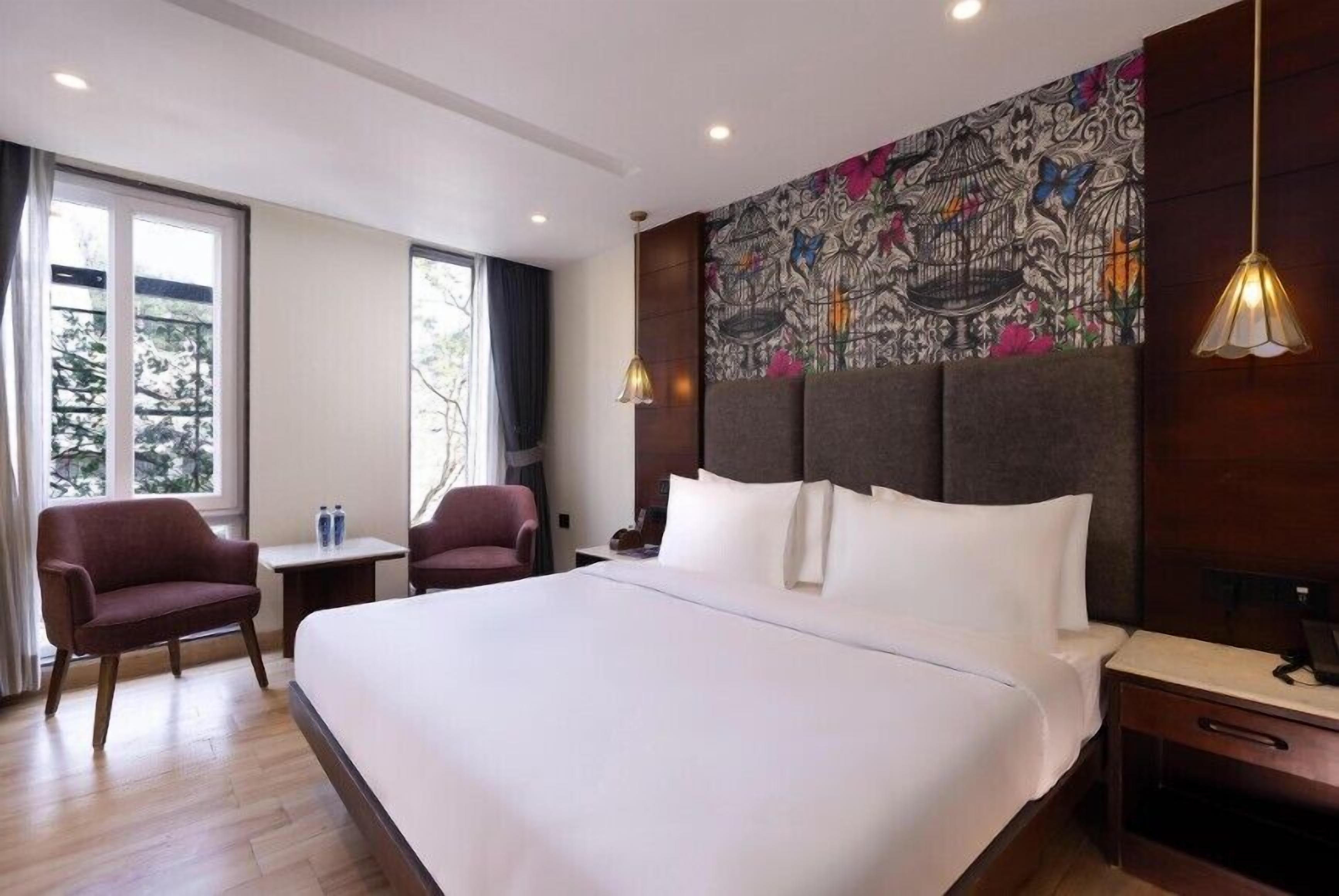 A hotel room with a large bed, two armchairs, a small table, and a decorative headboard.