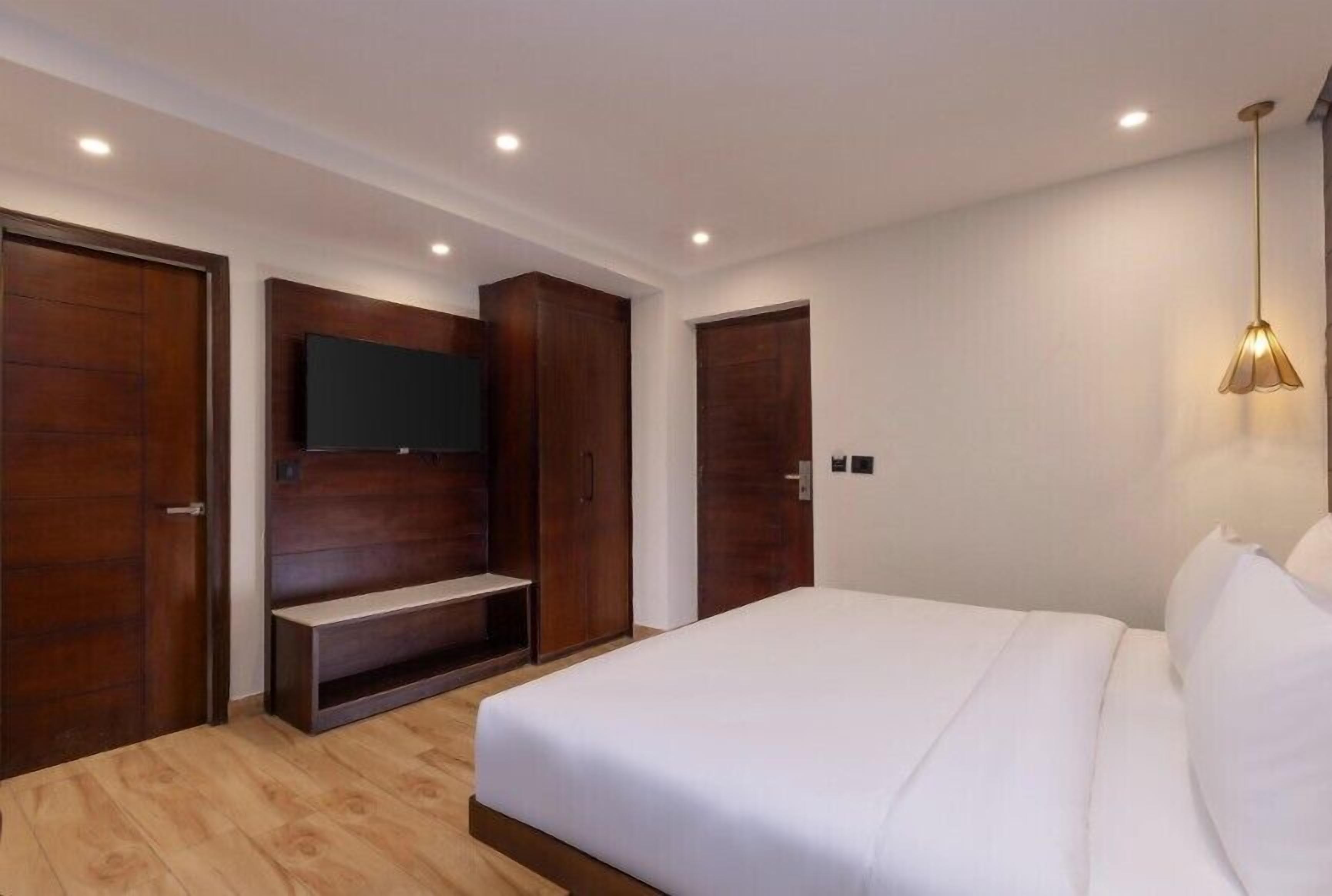 A bedroom with a bed, a TV mounted on a wooden panel, a wardrobe, and a pendant light.