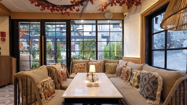 Un coin salon confortable avec un canapé et une table, de grandes fenêtres offrant une vue sur l’extérieur et des éléments décoratifs au plafond.