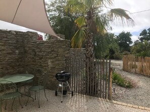 Eine Terrasse mit einer Steinmauer, einem runden Tisch mit Stühlen, einem Grill und einem Holzzaun.