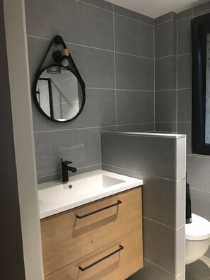 Ein modernes Badezimmer mit einem weißen Waschbecken, einem Holzkorpus und einem Spiegel.