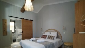 Une chambre à coucher avec un lit, une tête de lit en bois, un tabouret rond en bois et un luminaire suspendu.