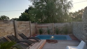 Un jardin avec une terrasse en bois, une piscine et deux chaises longues.