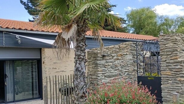 Une maison avec un mur en pierre, un palmier et une clôture en bois.