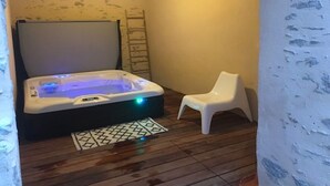 Une petite pièce avec un jacuzzi, une chaise en plastique blanche et une échelle appuyée contre le mur.