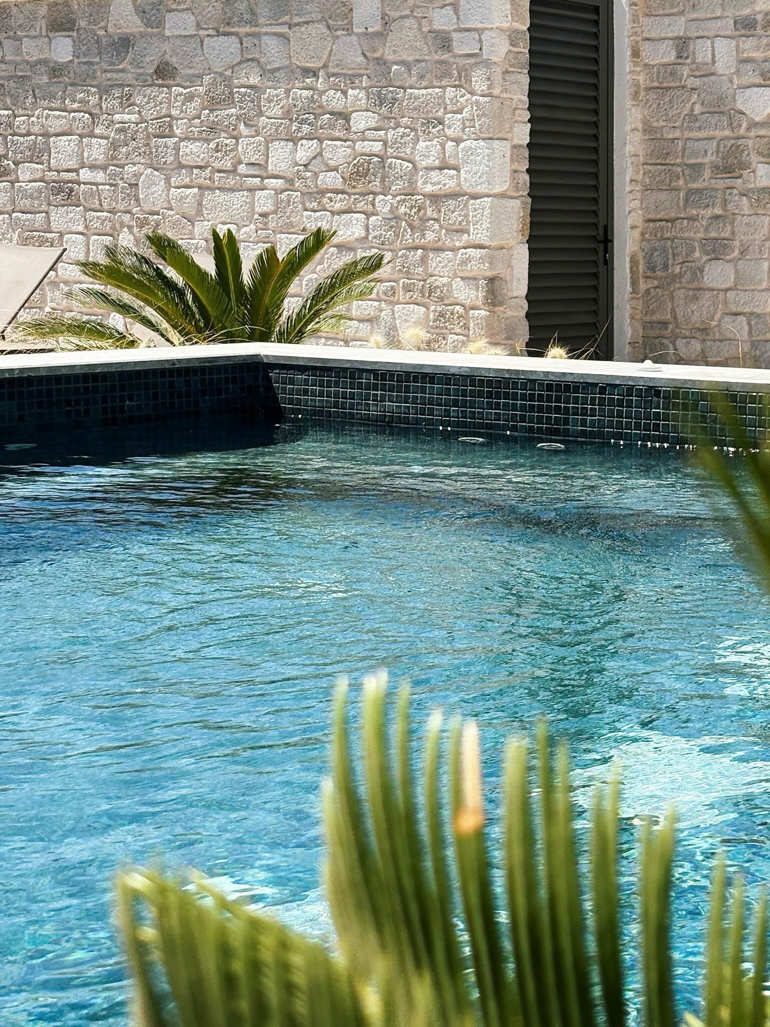 En swimmingpool med klart, blåt vand, omgivet af en stenvæg og en flisekant.