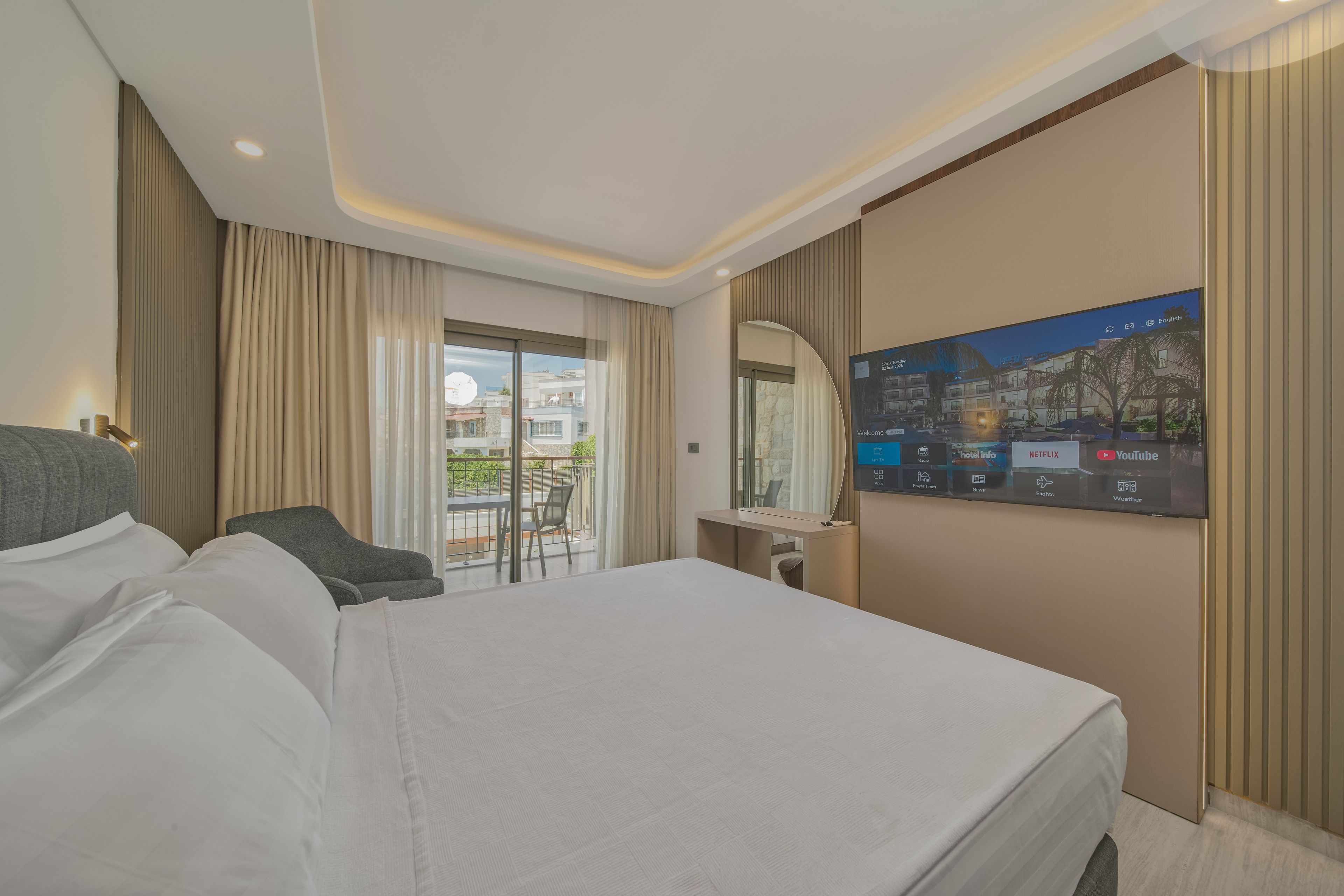 Una habitación de hotel con una cama grande, un escritorio, una silla, un televisor y un balcón con vistas a edificios.