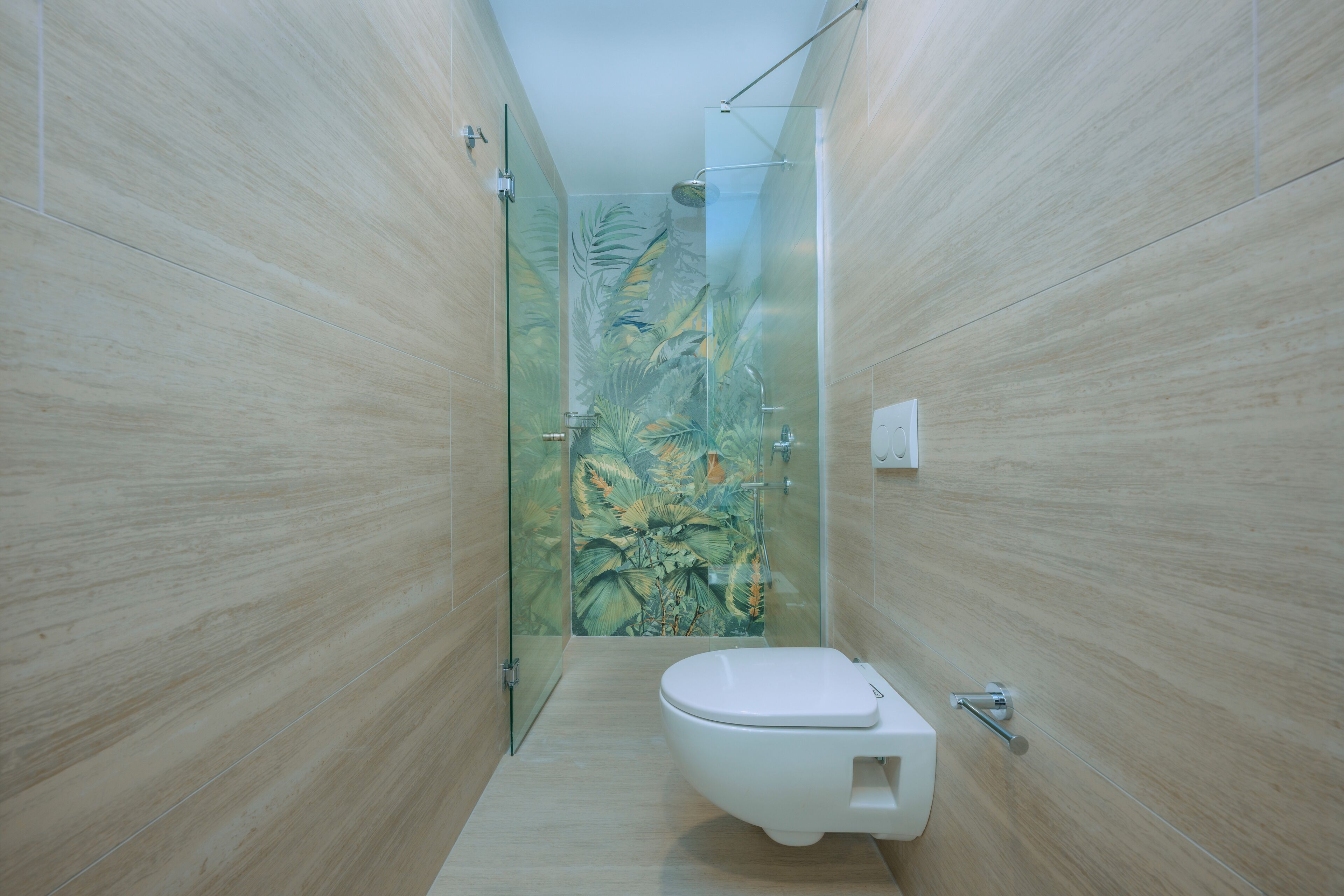 A narrow bathroom with a toilet, a glass shower enclosure, and a wall with a tropical mural.