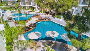 A large outdoor swimming pool with multiple lounge areas and umbrellas, surrounded by lush greenery and modern buildings. - Ayaz Suites (Bodrum)
