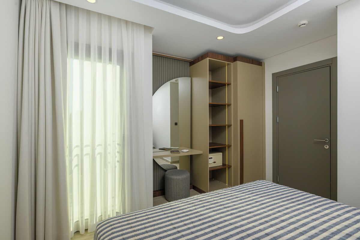A hotel room with a bed, a desk, a mirror, a wardrobe, and a door.