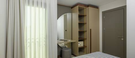 A hotel room with a bed, a desk, a mirror, a wardrobe, and a door.