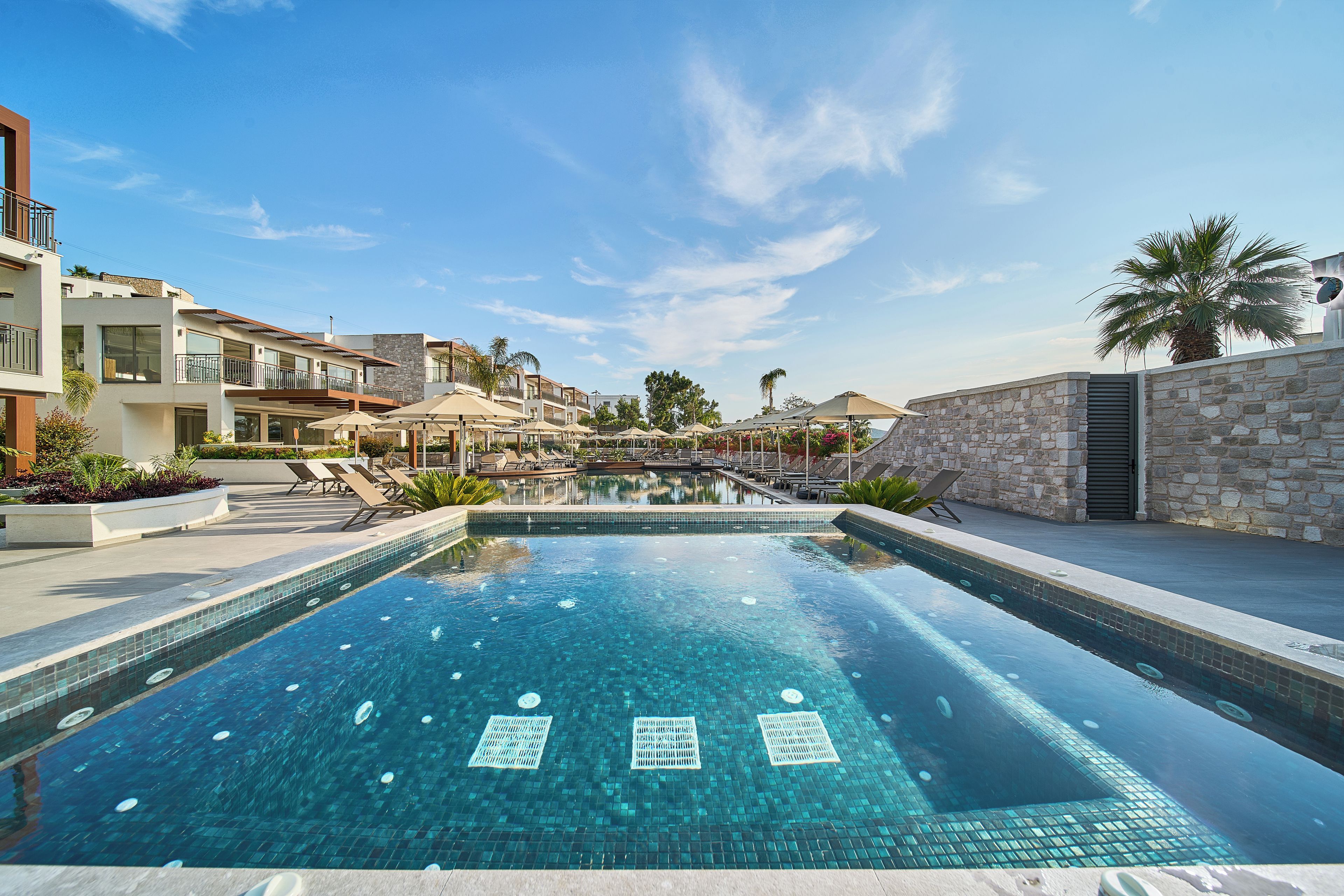 Una piscina con agua azul cristalina, rodeada de edificios modernos y palmeras.