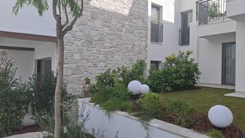 A courtyard with a stone wall, a tree, and a well-maintained garden with shrubs and spherical planters.