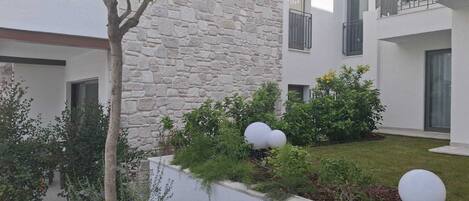 A courtyard with a stone wall, a tree, and a well-maintained garden with shrubs and spherical planters.