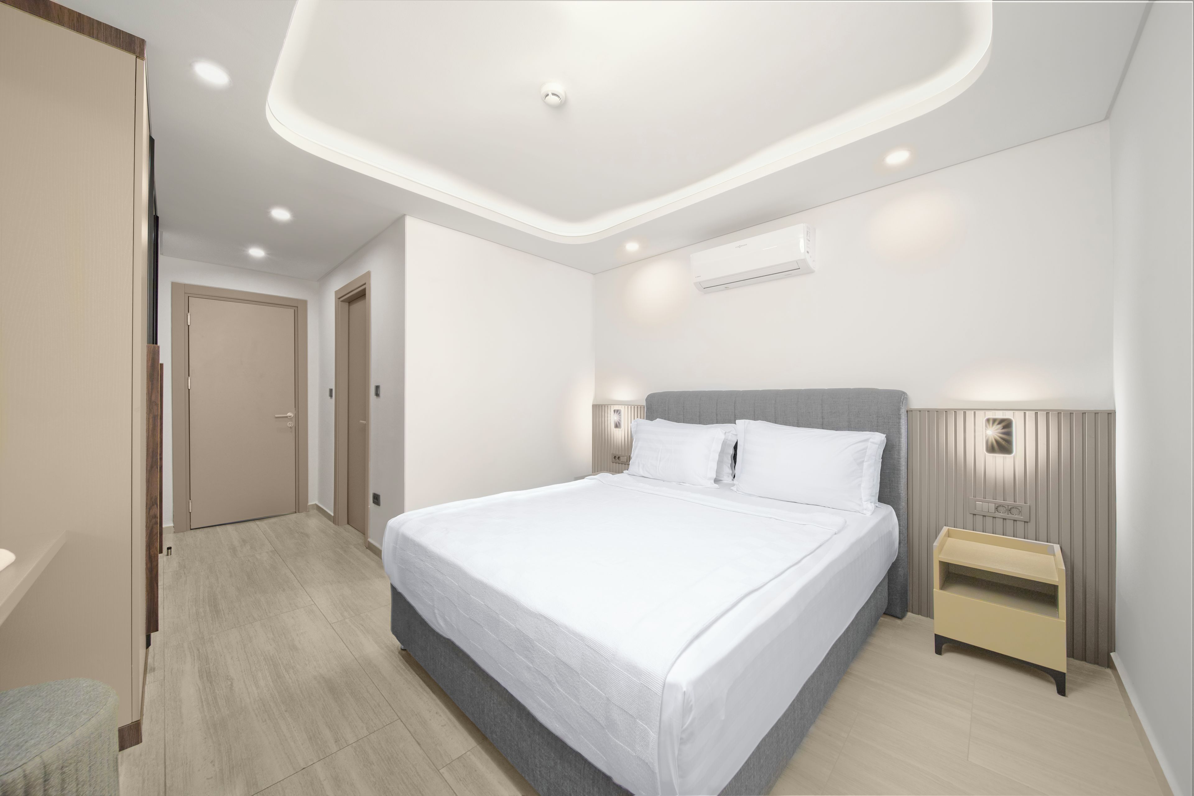 A modern hotel room with a large bed, bedside tables, a wardrobe, and an air conditioning unit.