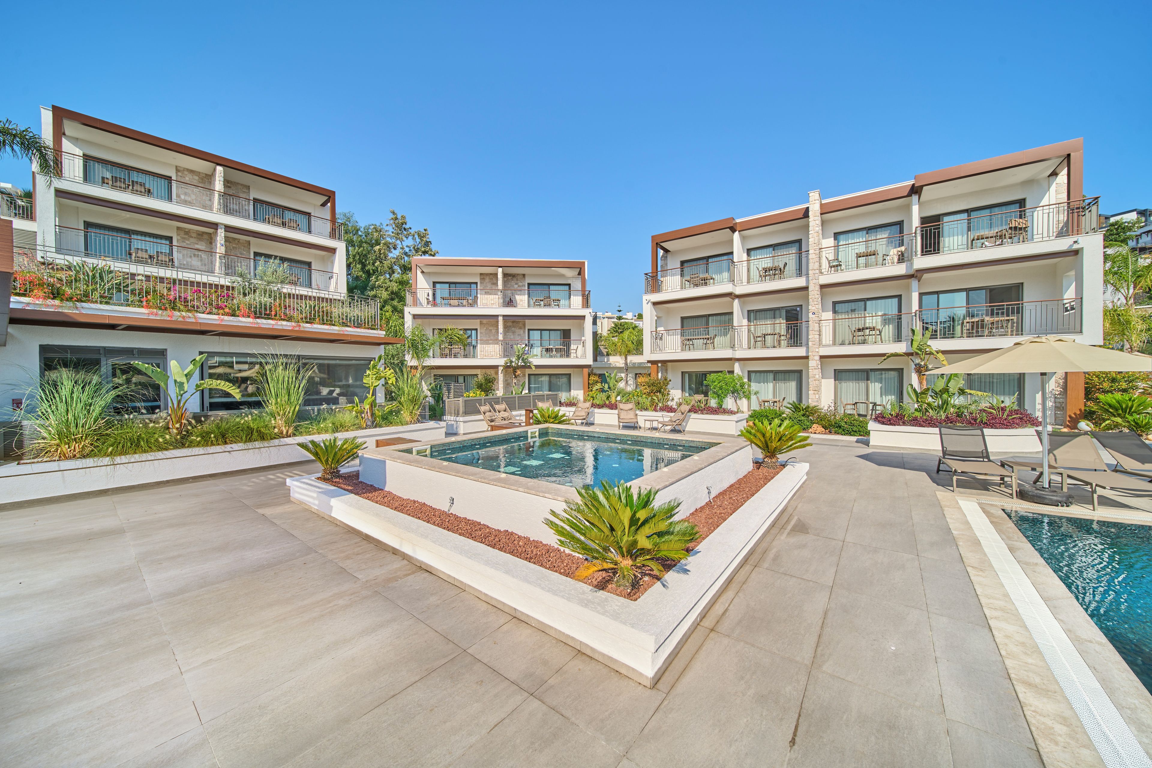 Un hotel moderno con piscina central, mobiliario exterior y balcones con muebles.