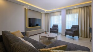 Un salon moderne avec un canapé, des fauteuils, une table basse et un téléviseur à écran plat.