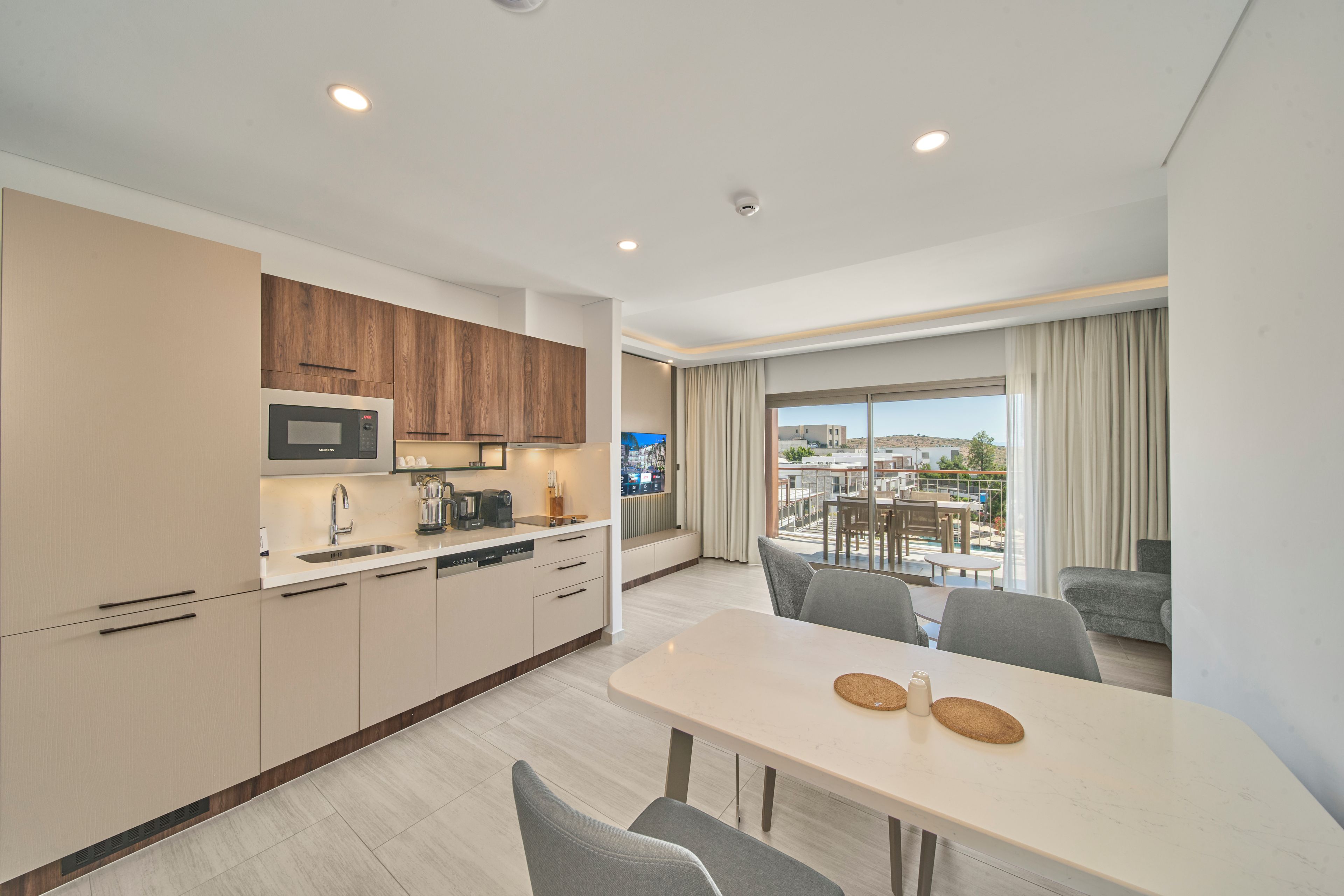 A modern kitchen with a Siemens microwave, a coffee machine, and a sink. There is a dining area with a table and chairs, and a view of a balcony with outdoor furniture.