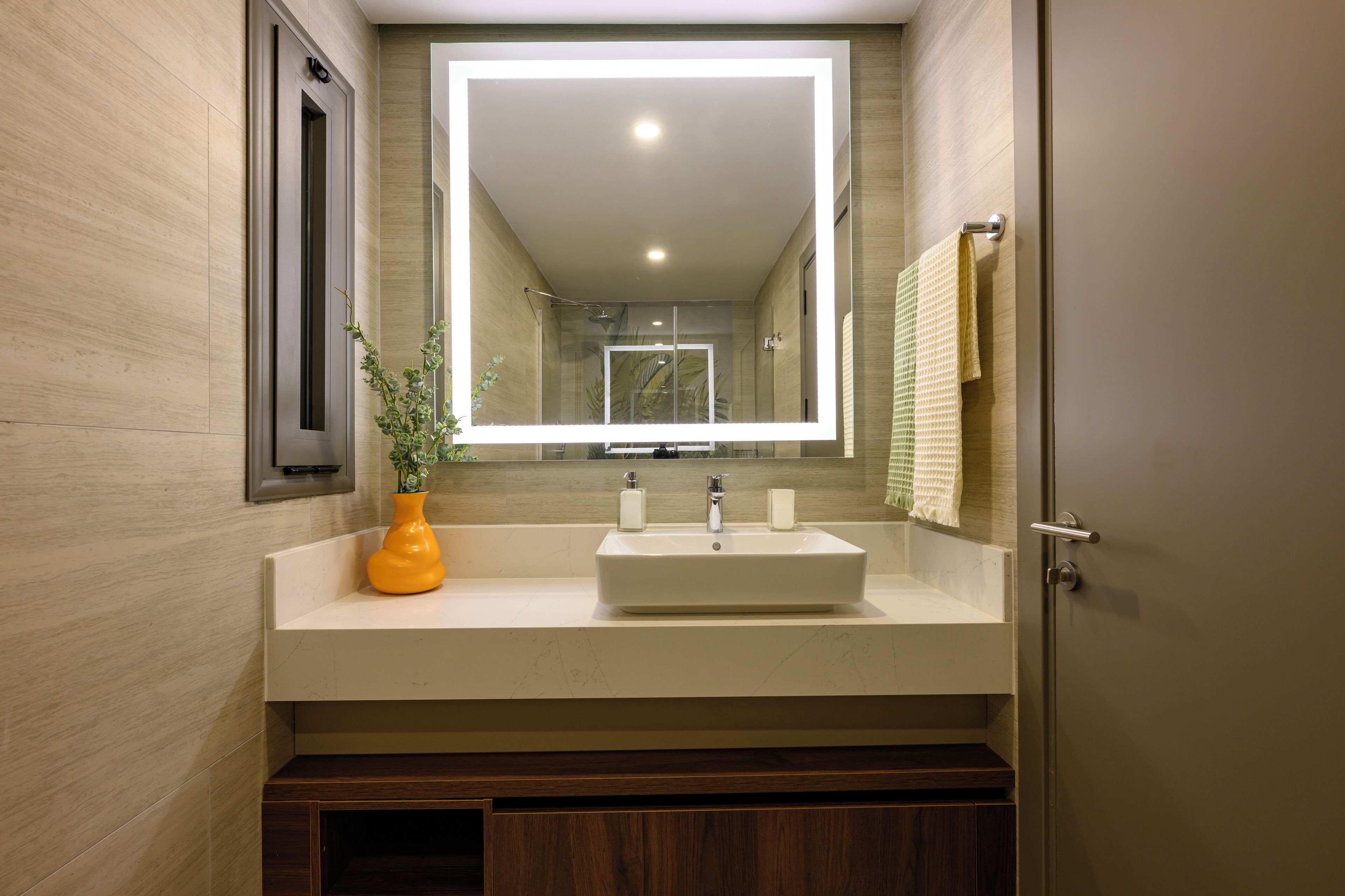 A modern bathroom with a large mirror, a white sink, and a yellow vase.