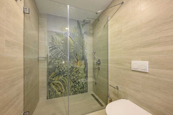 Un baño moderno con ducha de vidrio, paredes de azulejos y un inodoro.