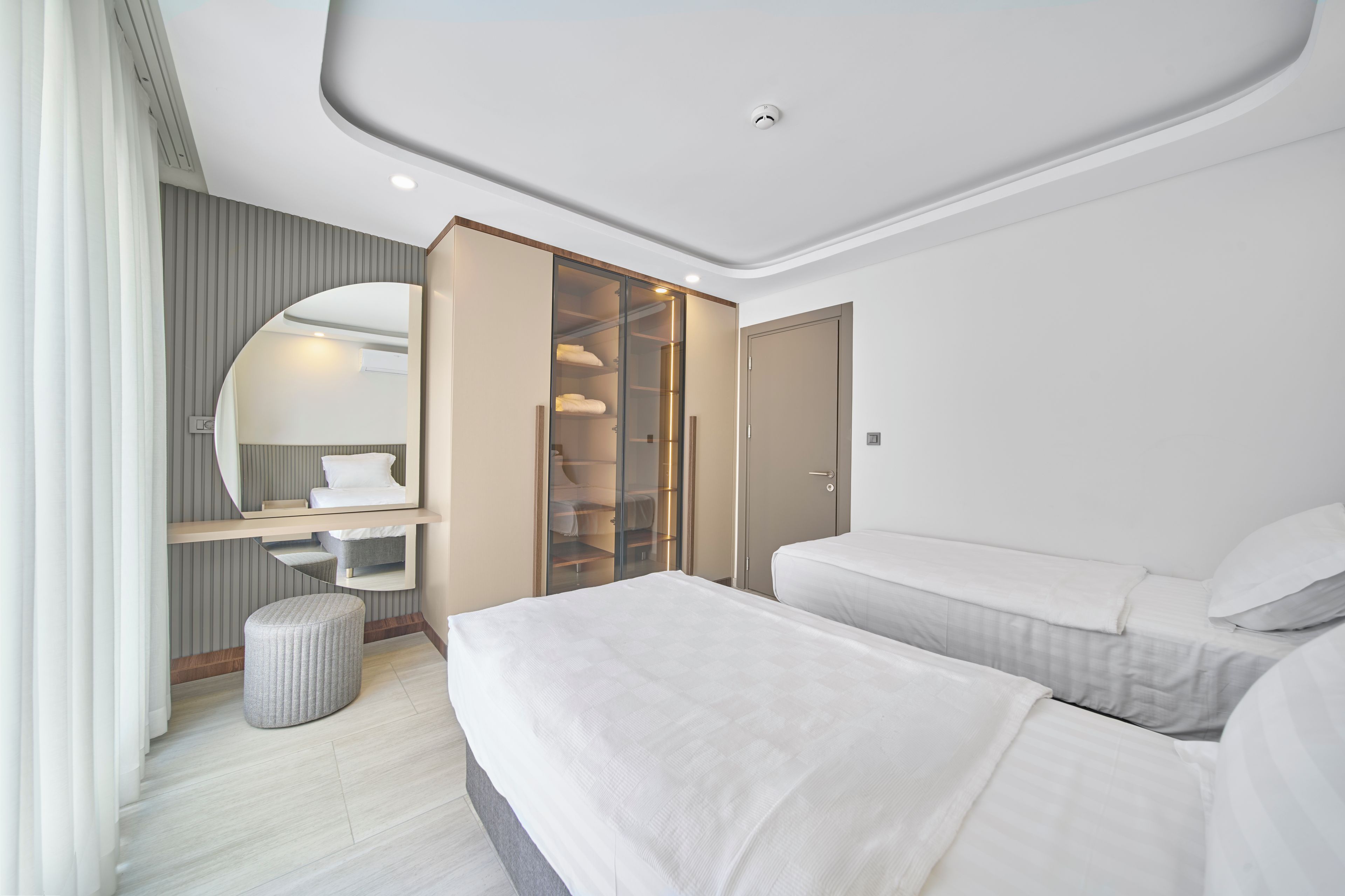 Un dormitorio moderno con cama, armario, espejo y un pequeño rincón de descanso.