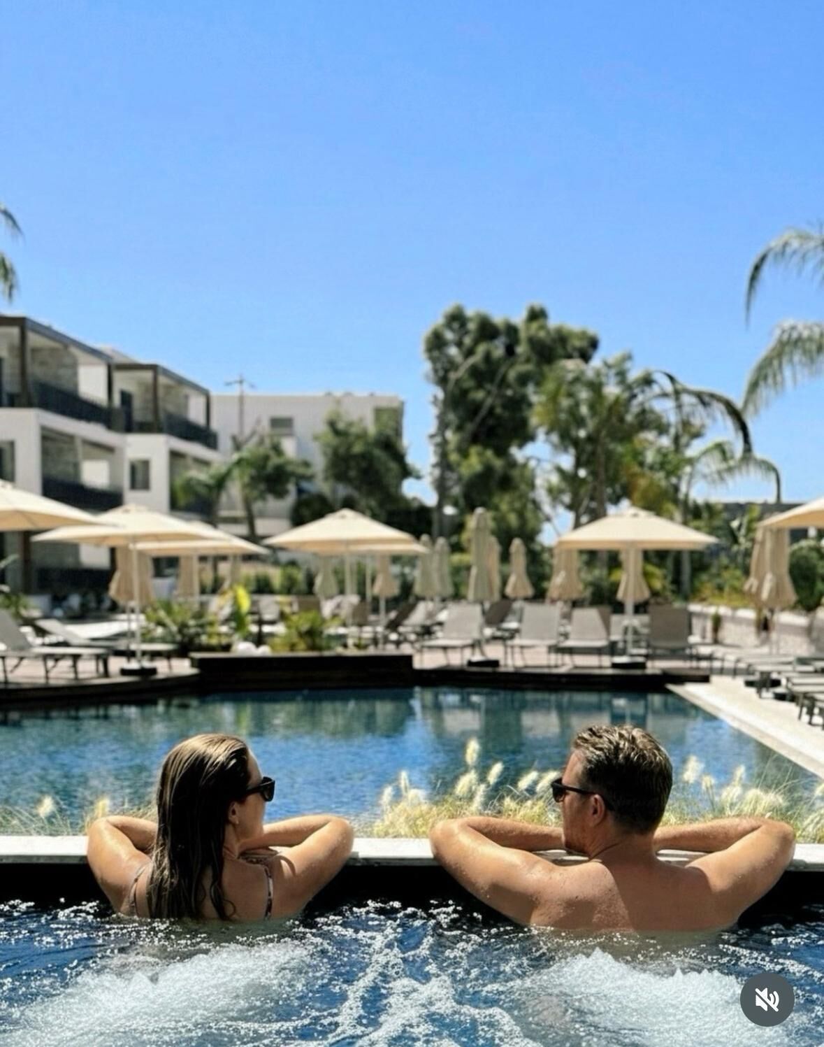 Un couple se détend dans un bain à remous, avec une piscine et des chaises longues en arrière-plan.