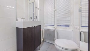 Un baño moderno con inodoro blanco, mueble de madera oscura y un espejo grande sobre el lavamanos.
