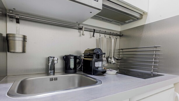 Una cocina con un lavamanos de acero inoxidable, una cafetera, un hervidor y una campana extractora.