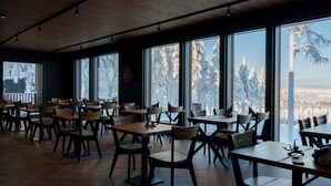 A restaurant with wooden tables and chairs, large windows with a snowy view. - Arctic Lumo Resort (Kuusamo)
