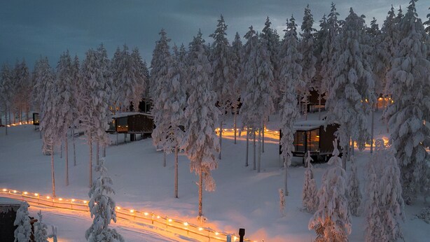 A modern, snow-covered lodge with glass-walled rooms, a hot tub, and a scenic snowy forest backdrop. - Arctic Lumo Resort (Kuusamo)