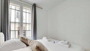 A hotel room with a bed, pillows, a window with curtains, and a view of buildings outside. - Cosy Apartment - 1br/4p - Place de la Nation (Paris)