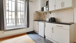 A kitchen with white cabinets, a black countertop, and a microwave. - Cosy Apartment - 1br/4p - Place de la Nation (Paris)