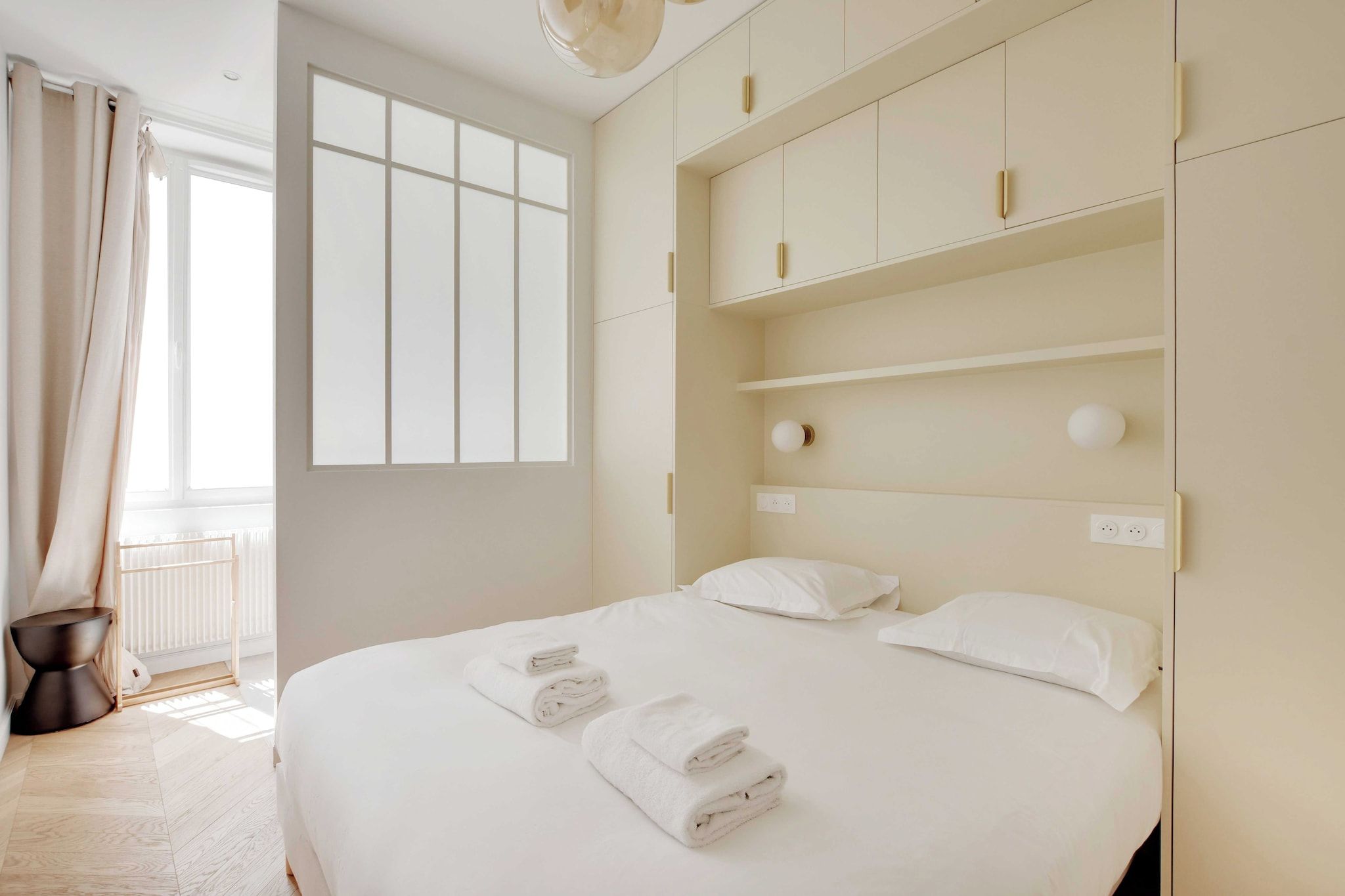 A hotel room with a large bed, white linens, a bedside table, a radiator, and a window with curtains.