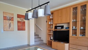 A modern living room with a glass coffee table, a sofa, a TV, and wooden cabinets with glass doors.