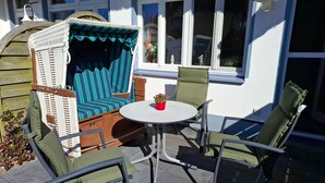 A patio with a wicker sofa, green cushioned chairs, and a small table with a potted plant.