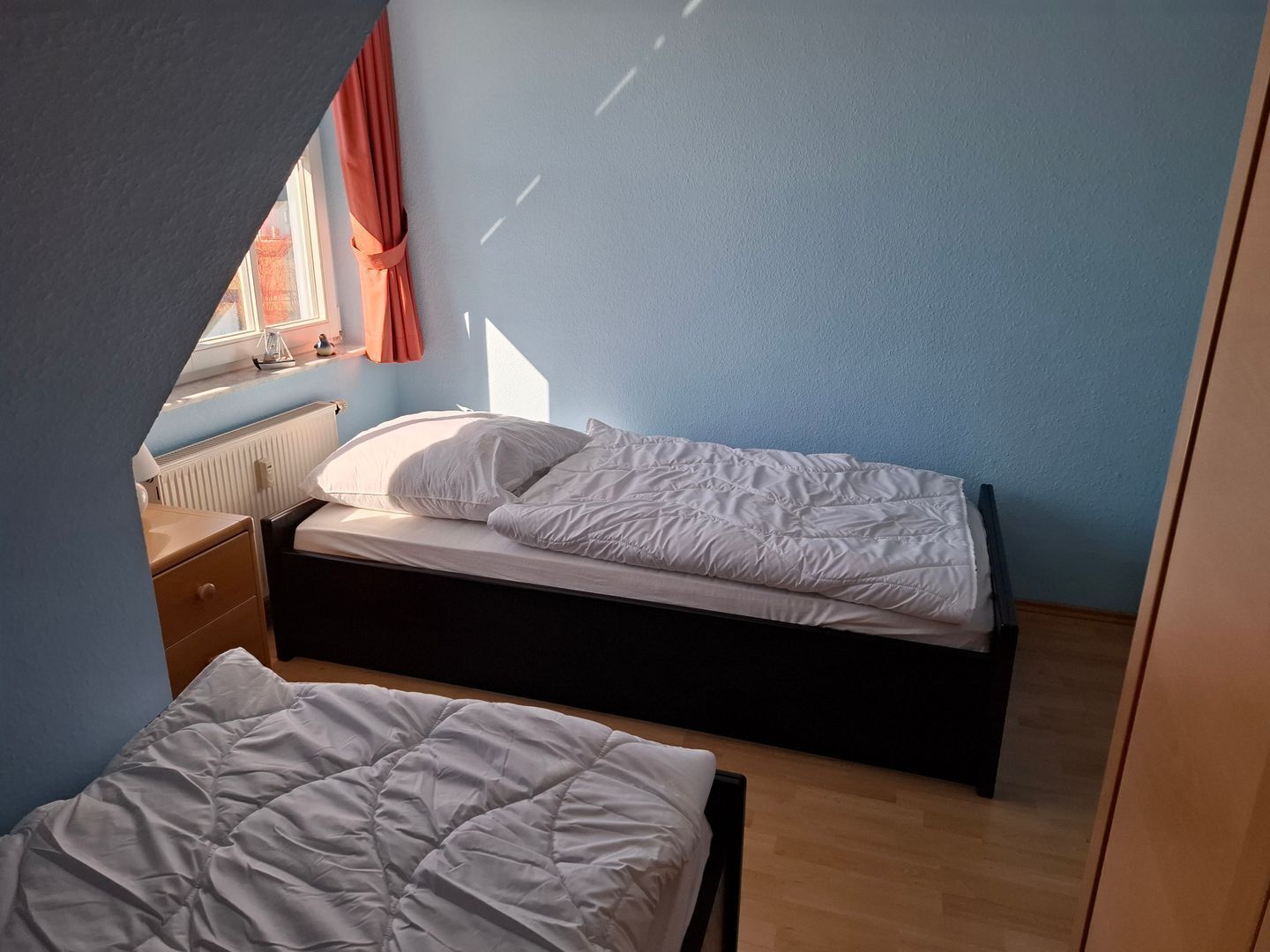 Une petite chambre avec un lit simple, une fenêtre, un radiateur et un plancher en bois.