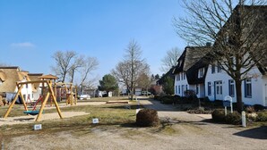 A playground with swings and a slide, a gravel path, and houses with white walls and dark shutters.