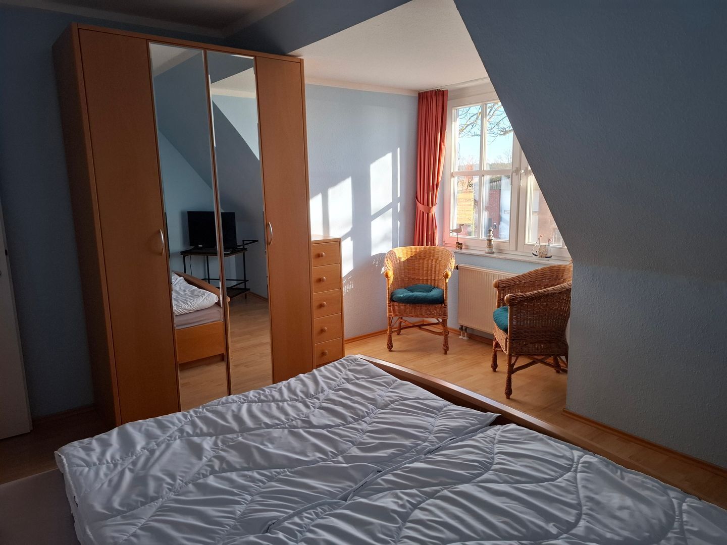 Un dormitorio con una cama, un armario, un escritorio y dos sillas de mimbre.