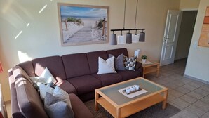 A living room with a brown sofa, a glass coffee table, and a painting of a beach scene.
